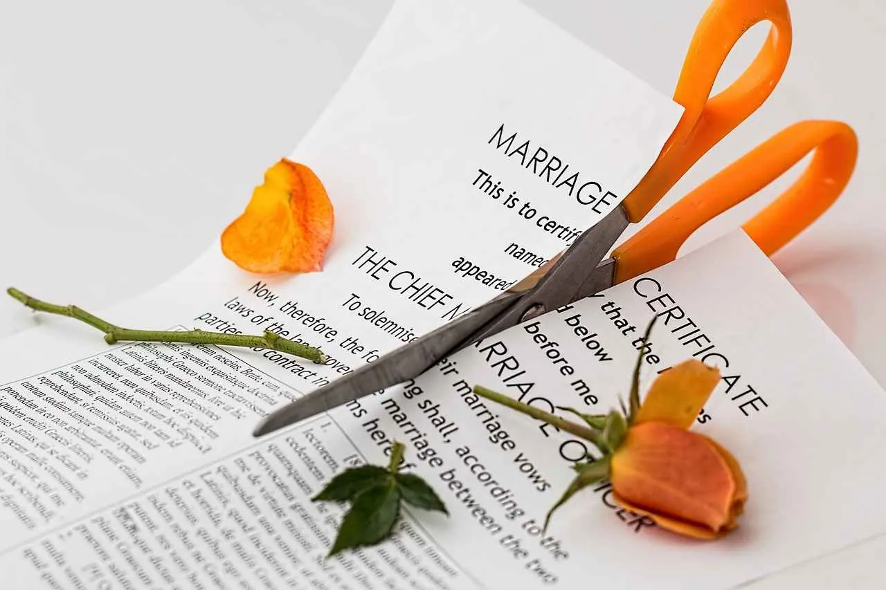 Orange-handled scissors cutting a marriage certificate with a torn orange rose.