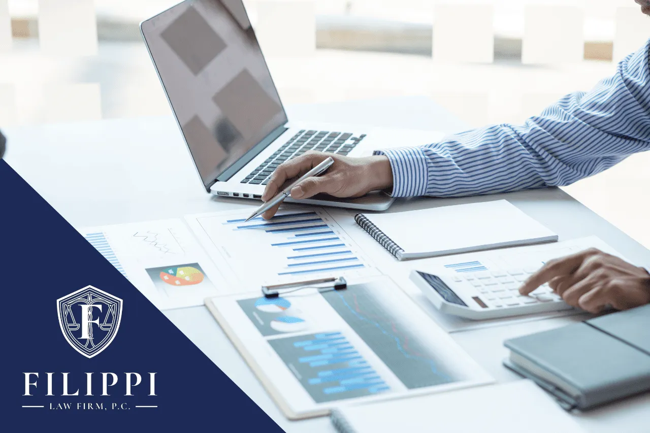 Professional working at desk with laptop, financial charts, calculator, and Filippi Law Firm logo.