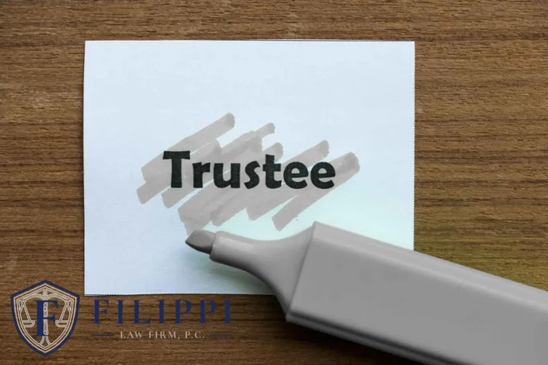 White card with the word "Trustee" highlighted by a gray marker on a wooden surface, Filippi Law Firm logo.