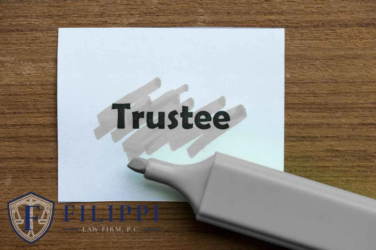 White card with the word "Trustee" highlighted by a gray marker on a wooden surface, Filippi Law Firm logo.