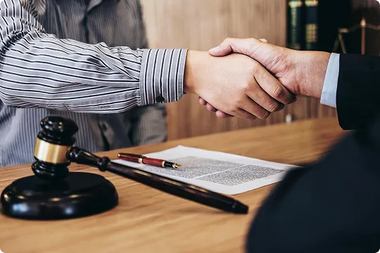 Two individuals shaking hands over a wooden desk with legal documents and a gavel.
