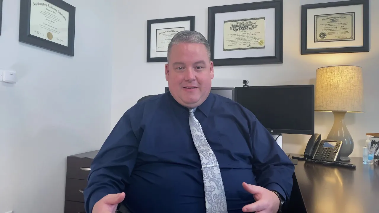 Man in navy blue shirt and paisley tie seated at desk with framed diplomas and certificates behind.