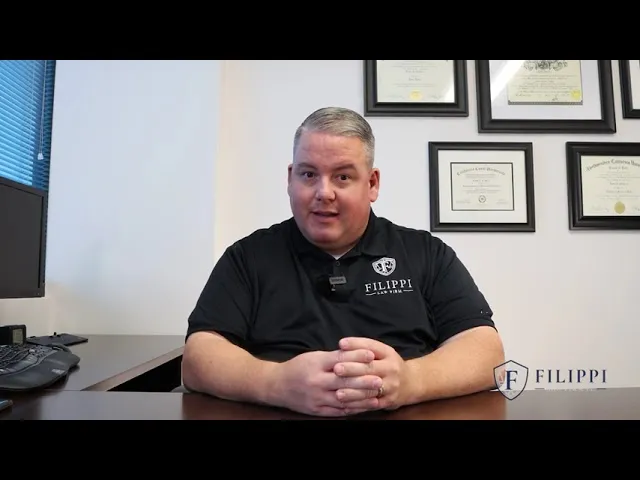 Man in black Filippi Law Firm polo seated at desk with framed certificates on wall behind.