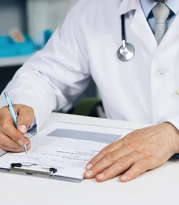 Doctor in white coat with stethoscope writing on a medical form on clipboard.