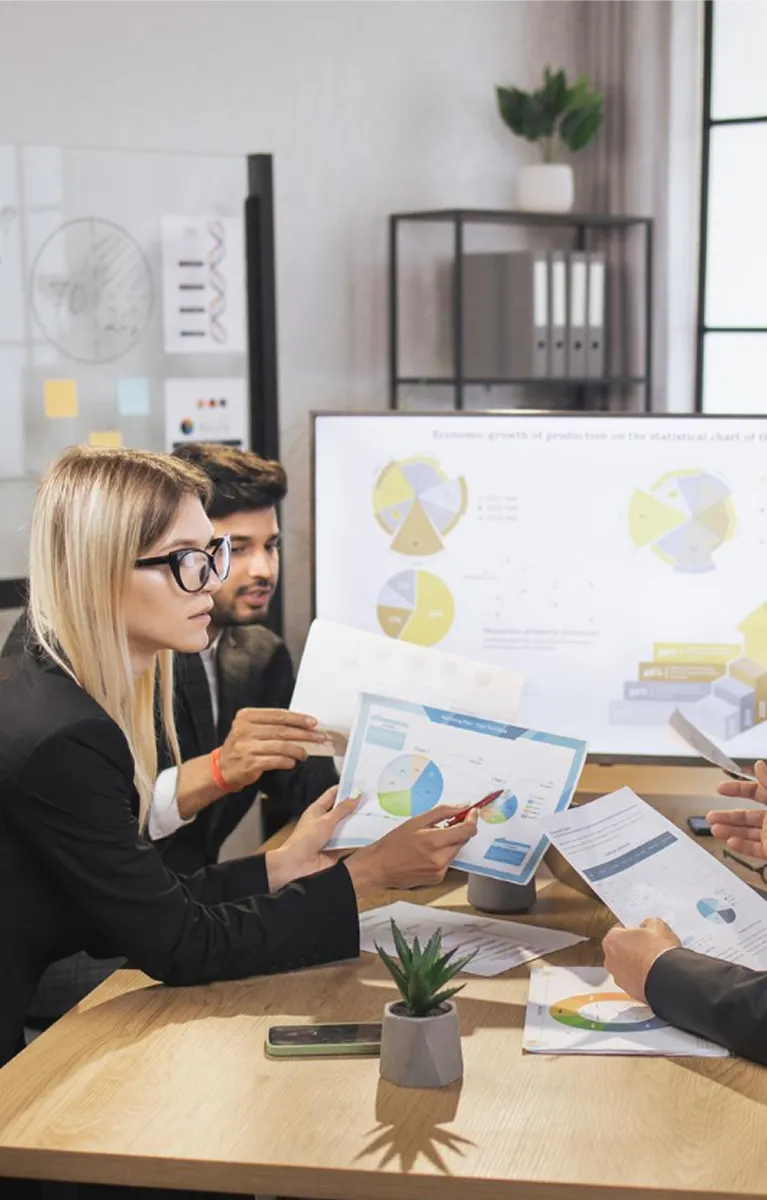 Three professionals reviewing charts and graphs during a business meeting in an office.
