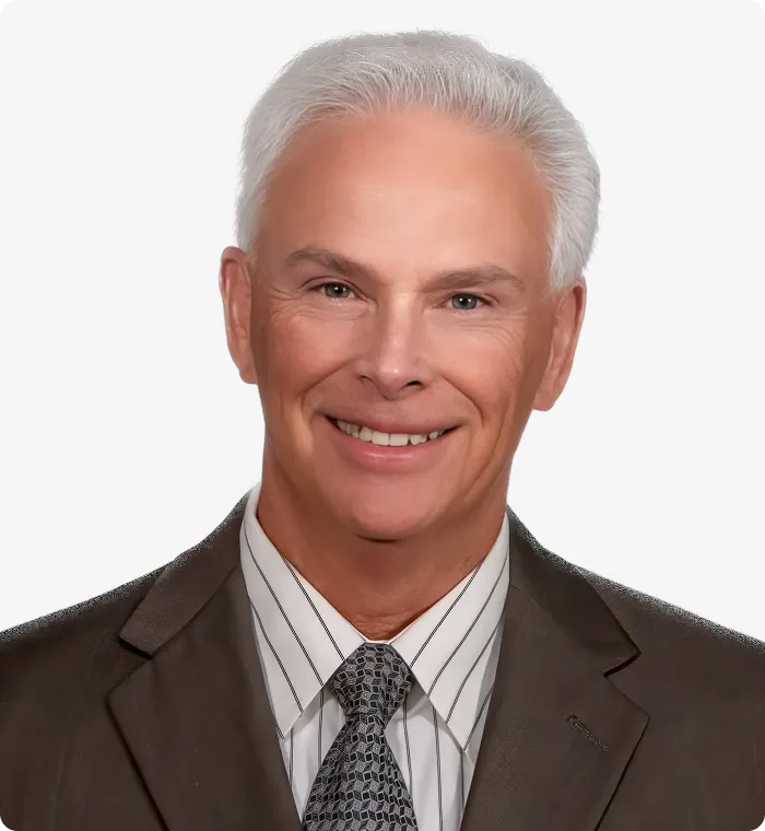 Professional headshot of a smiling mature man with white hair wearing a suit and patterned tie.
