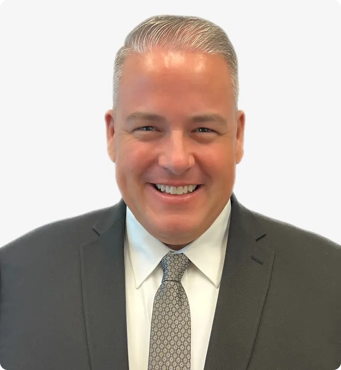 Portrait of a smiling man in a dark suit, white shirt, and patterned tie against white background.