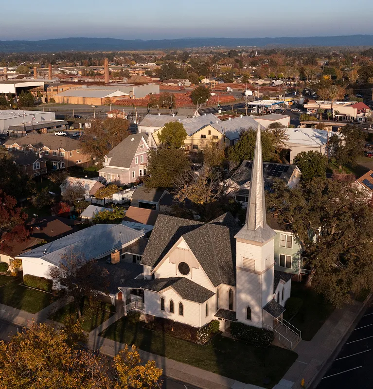 Aerial view of a white church with a tall steeple surrounded by residential houses and trees.
