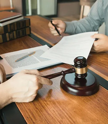 Two individuals reviewing legal documents at a wooden table with a judge's gavel.