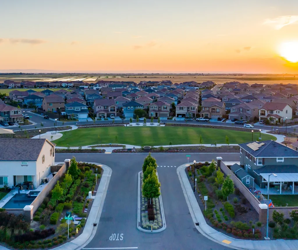 Aerial view of suburban neighborhood with houses surrounding a central green park at sunset.