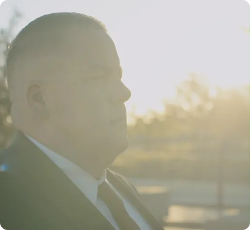Profile view of a man in formal attire with bright sunlight in the background.