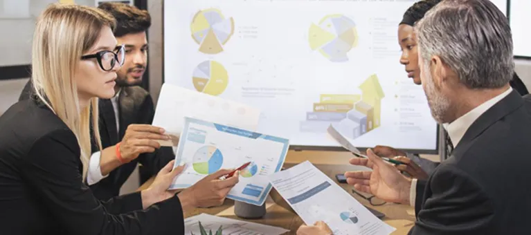 Four business professionals reviewing charts and graphs during a meeting.