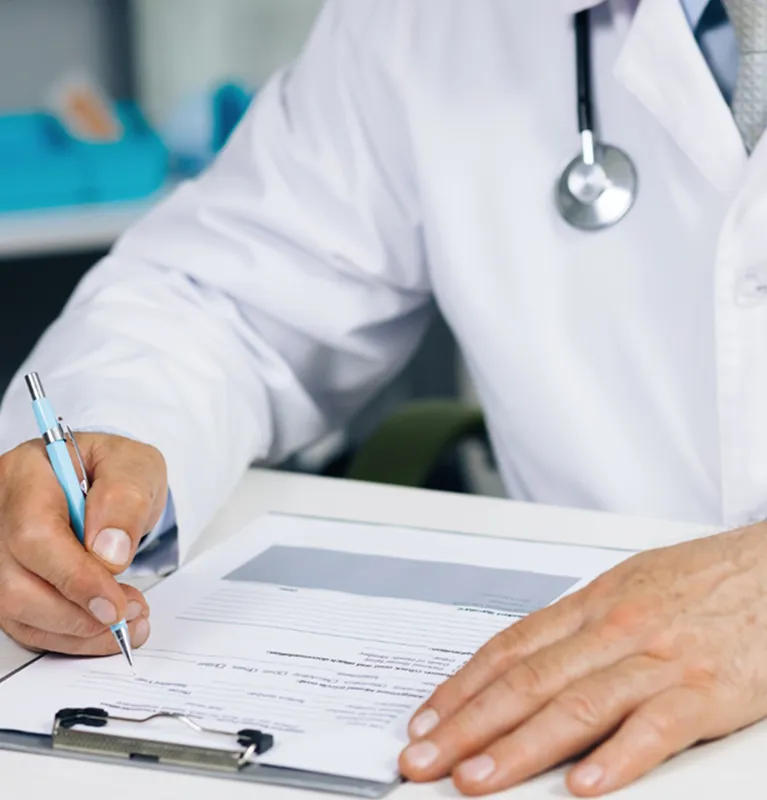 Medical professional in white coat writing on a clipboard with a blue pen.