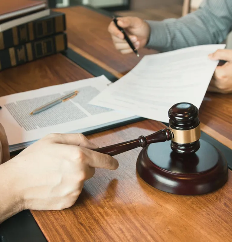 Hand holding wooden judge's gavel on table with legal documents and pen.