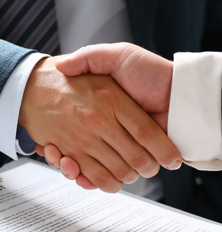 Close-up of two individuals in formal attire shaking hands over a contract document.