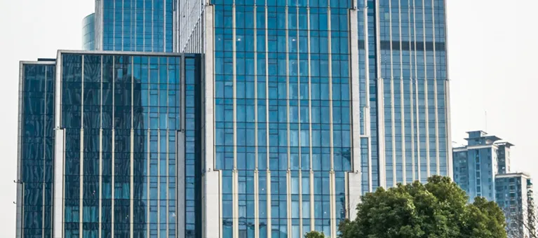 Modern glass skyscrapers with reflective blue windows and green trees in the foreground.