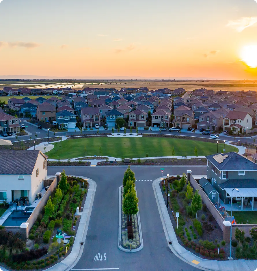 Aerial view of suburban neighborhood at sunset with houses, green park, and landscaped streets.