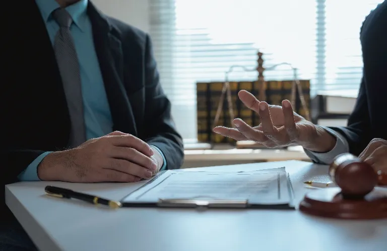 Two professionals in suits discussing documents at a desk with legal symbols.
