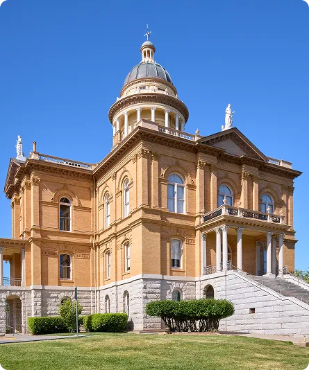Exterior view of a historic beige stone courthouse with a central dome and statues against a clear blue sky.