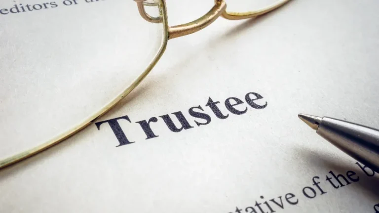 Close-up of a document with the word "Trustee," accompanied by a gold-rimmed eyeglass frame and a silver pen.