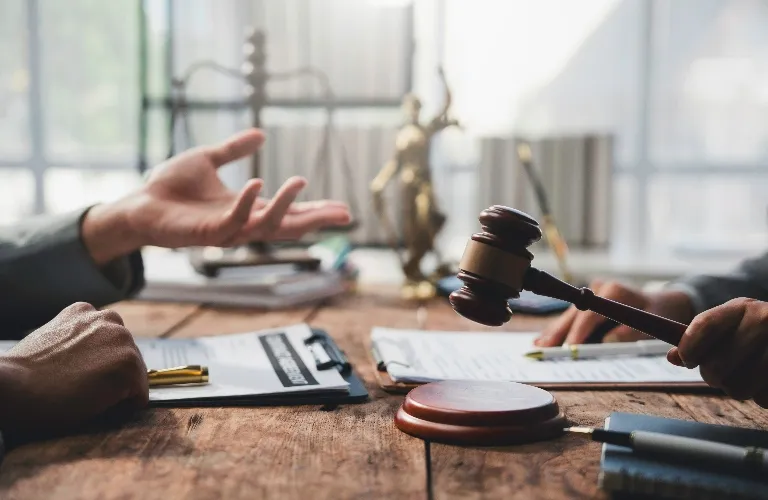 Close-up of two people discussing legal documents at a wooden table with a judge's gavel and Lady Justice statue in the background.