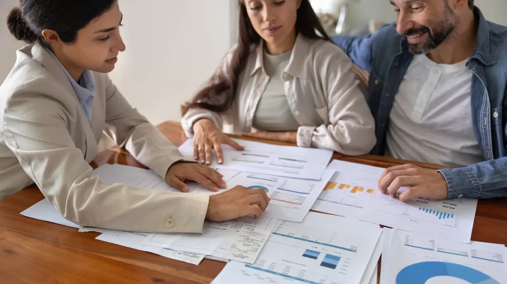 Three professionals reviewing and discussing financial charts and documents on a wooden table.