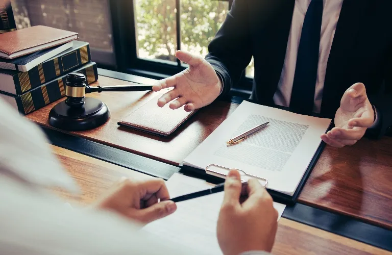 Two professionals in formal attire discussing documents at a wooden desk with legal books and a gavel.