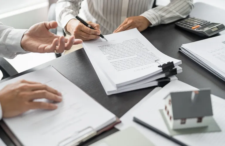 Two professionals reviewing and signing documents at a black office desk.