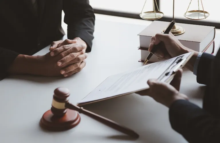 Two individuals in formal attire at a desk with legal documents, a gavel, and scales of justice.
