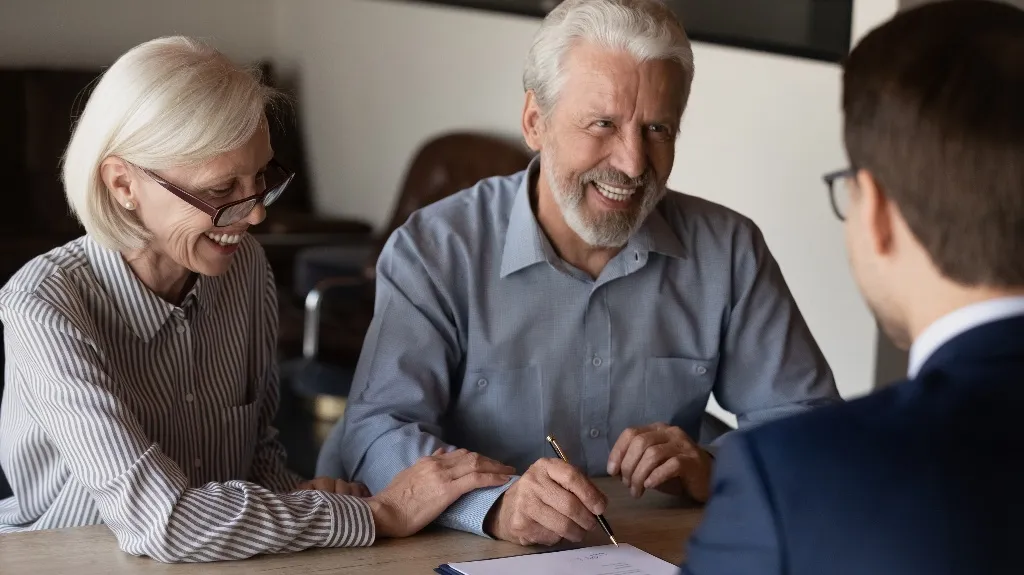 Elderly couple smiling and signing documents while consulting with a professional.