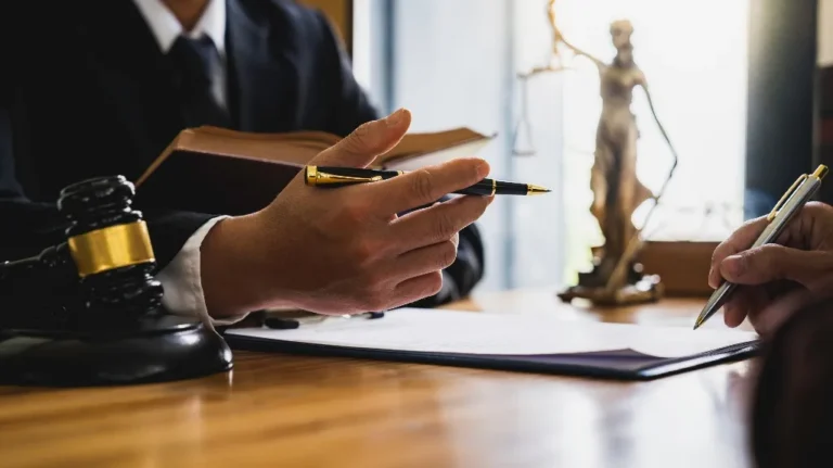 Two individuals in formal attire discussing legal documents with a judge's gavel and Lady Justice statue on a wooden desk.