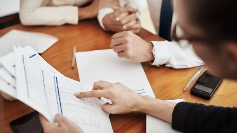 Two professionals reviewing printed documents and charts at a wooden table.