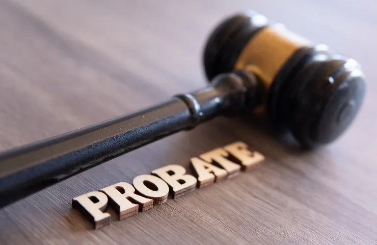 Wooden gavel resting on a surface next to the word "PROBATE" spelled in wooden letters.