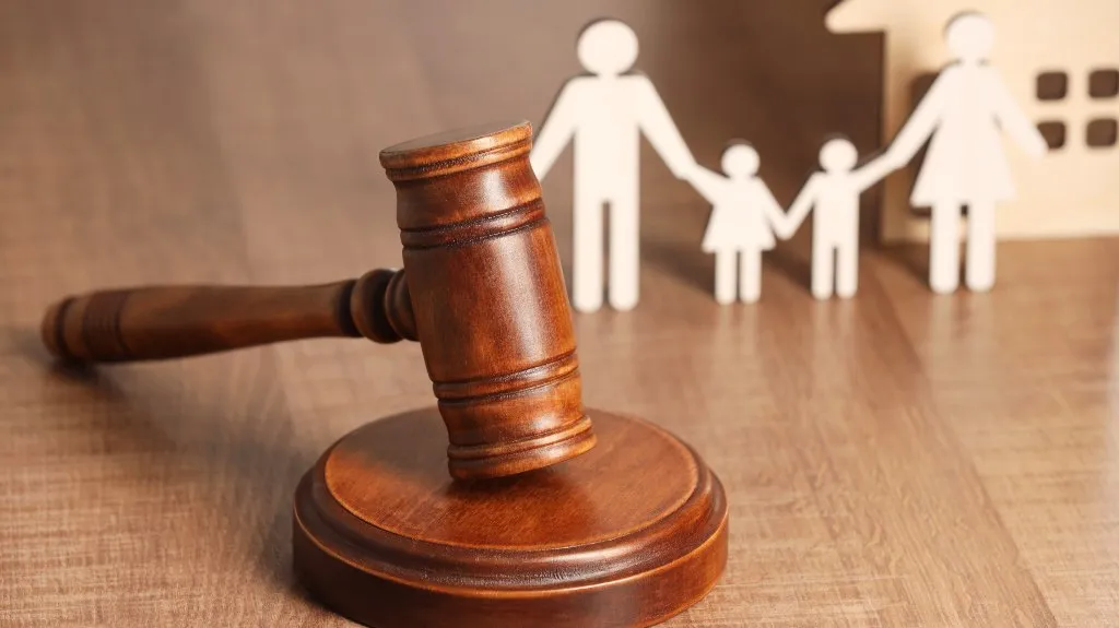 Wooden judge's gavel in foreground with paper cutout family and house in background.