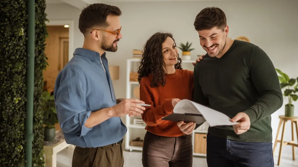 Three colleagues in casual attire reviewing documents and smiling in a modern office.