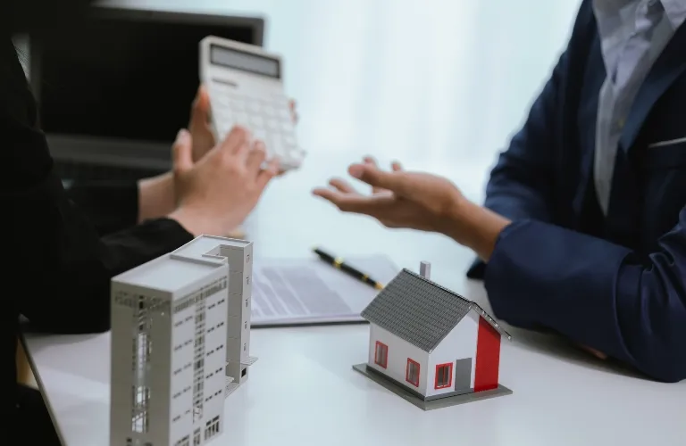 Two professionals discussing real estate with building and house models on table.
