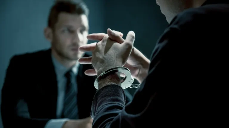 Two men in a dimly lit room, one handcuffed, engaged in a serious conversation.