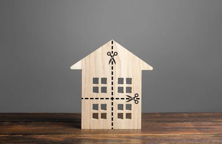 Wooden house model on wooden surface with black dashed lines and scissors icons.